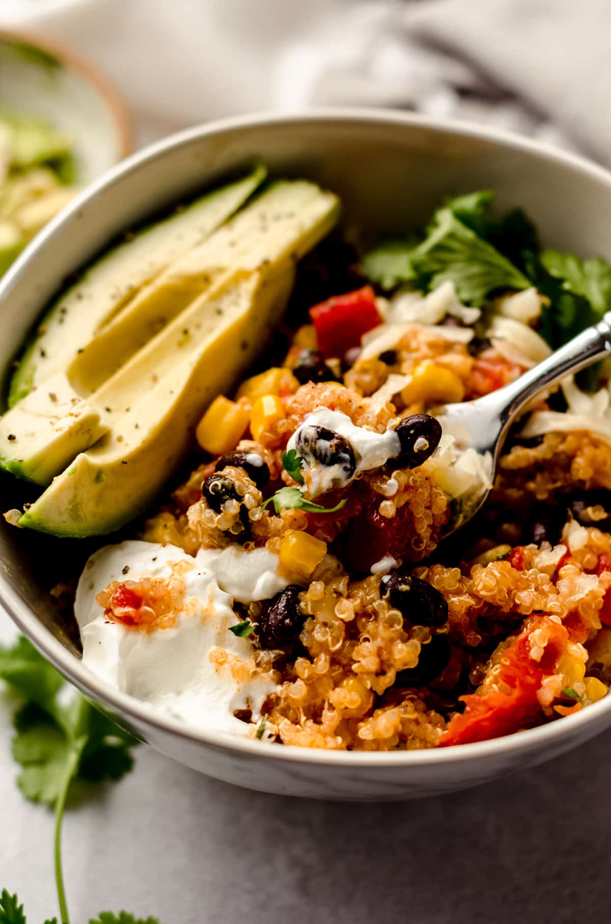 enchilada quinoa casserole in a bowl with sliced avocado, sour cream, and a fork