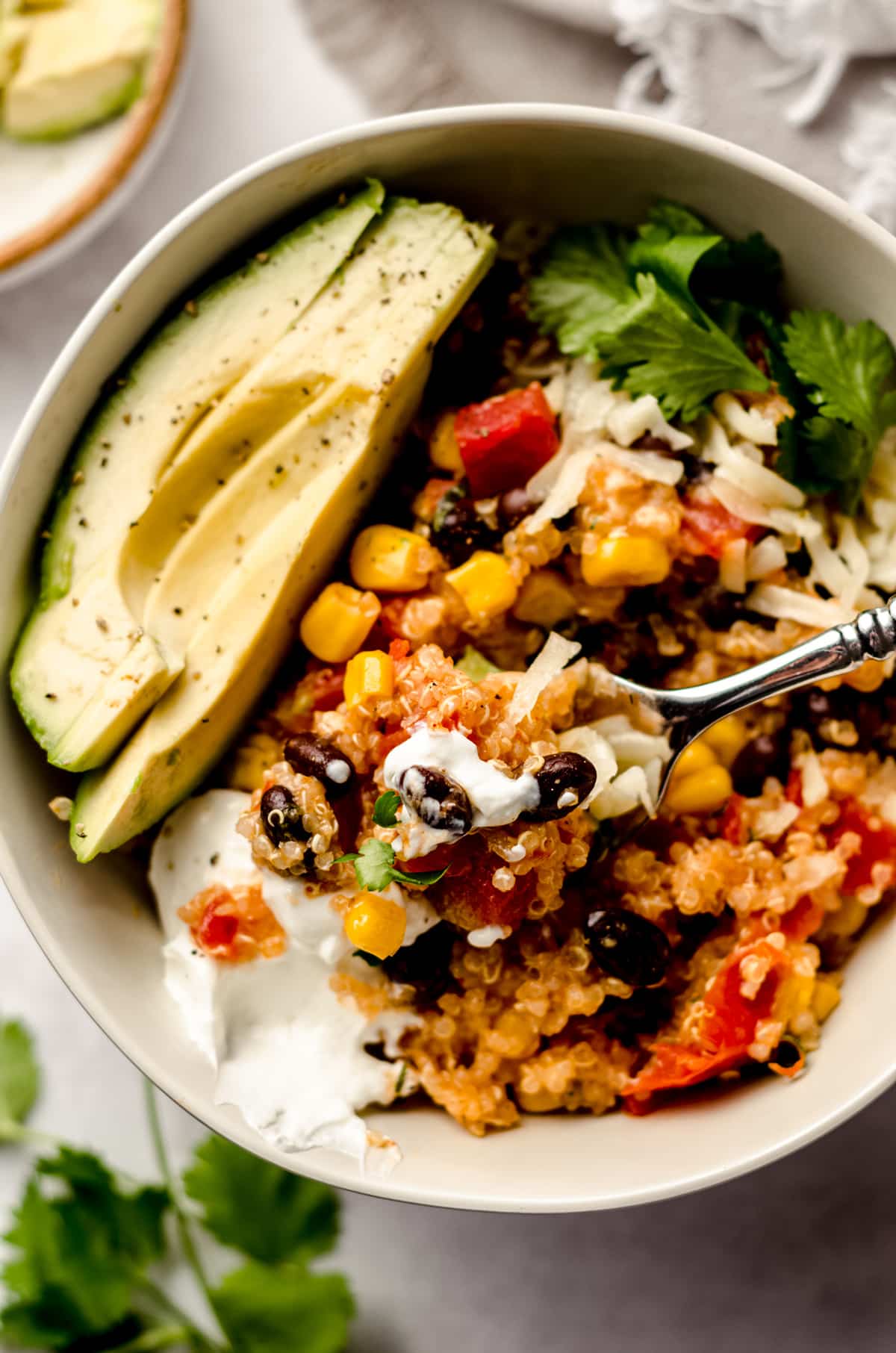 enchilada quinoa casserole in a bowl with sliced avocado, sour cream, and a fork