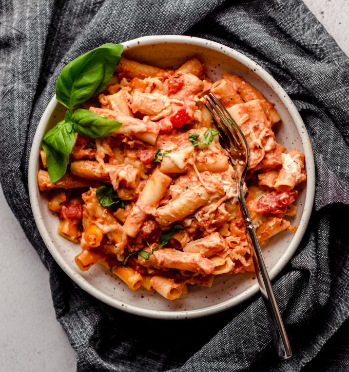 An aerial photo of a bowl of baked ziti with a sprig of basil.