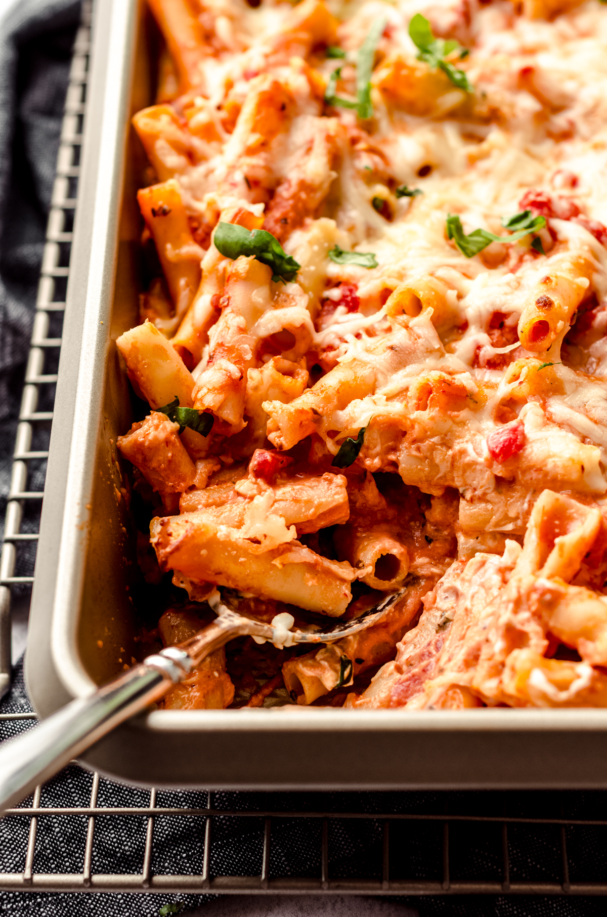 A serving spoon in a casserole dish of baked ziti.