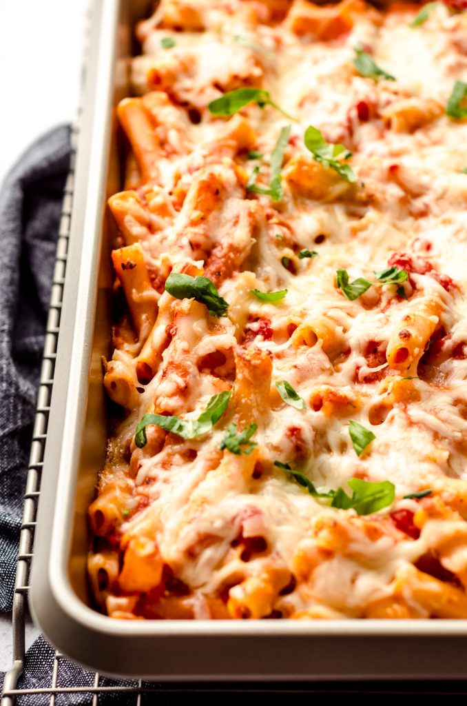 Baked ziti in a casserole dish topped with shredded basil.
