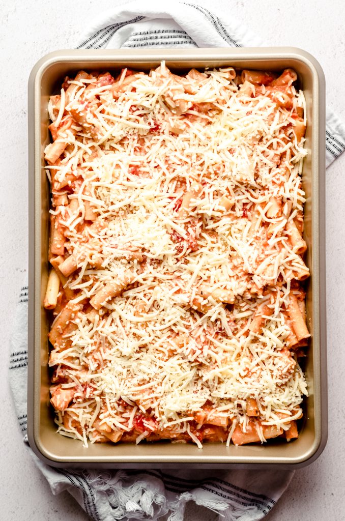 Aerial photo of baked ziti in a casserole dish topped with shredded cheese.