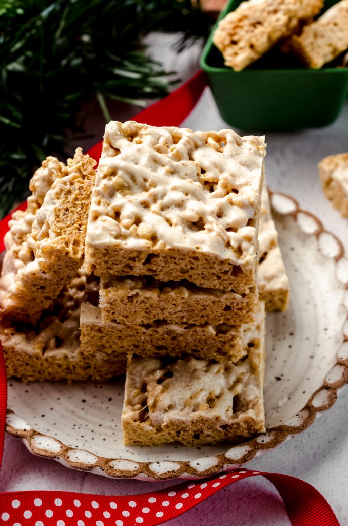 A stack of gingerbread Rice Krispies treats on a plate with Christmas fern and ribbon around it.