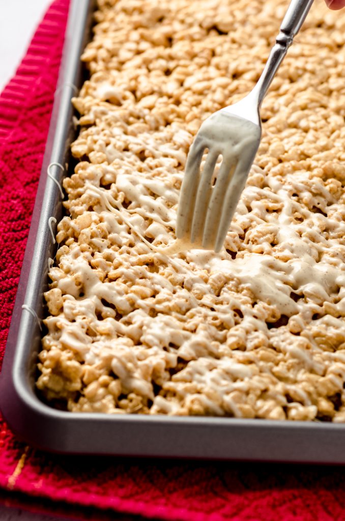 Someone is using a fork to drizzle gingerbread Rice Krispies treats with spiced white chocolate.