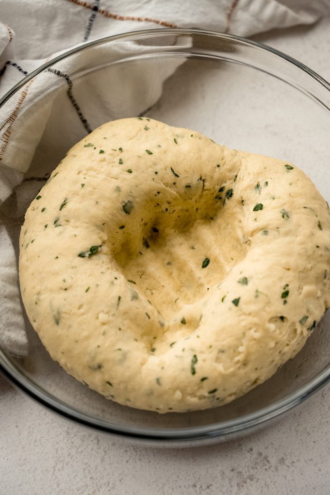 Parmesan parsley yeast bread dough that has been punched down in a large glass bowl.