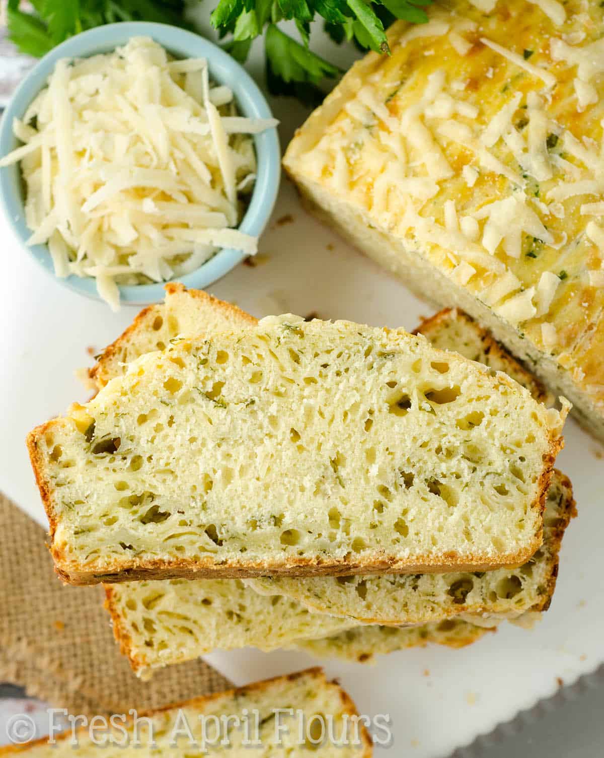 A loaf of parmesan parsley bread sliced and stacked on a cutting board.