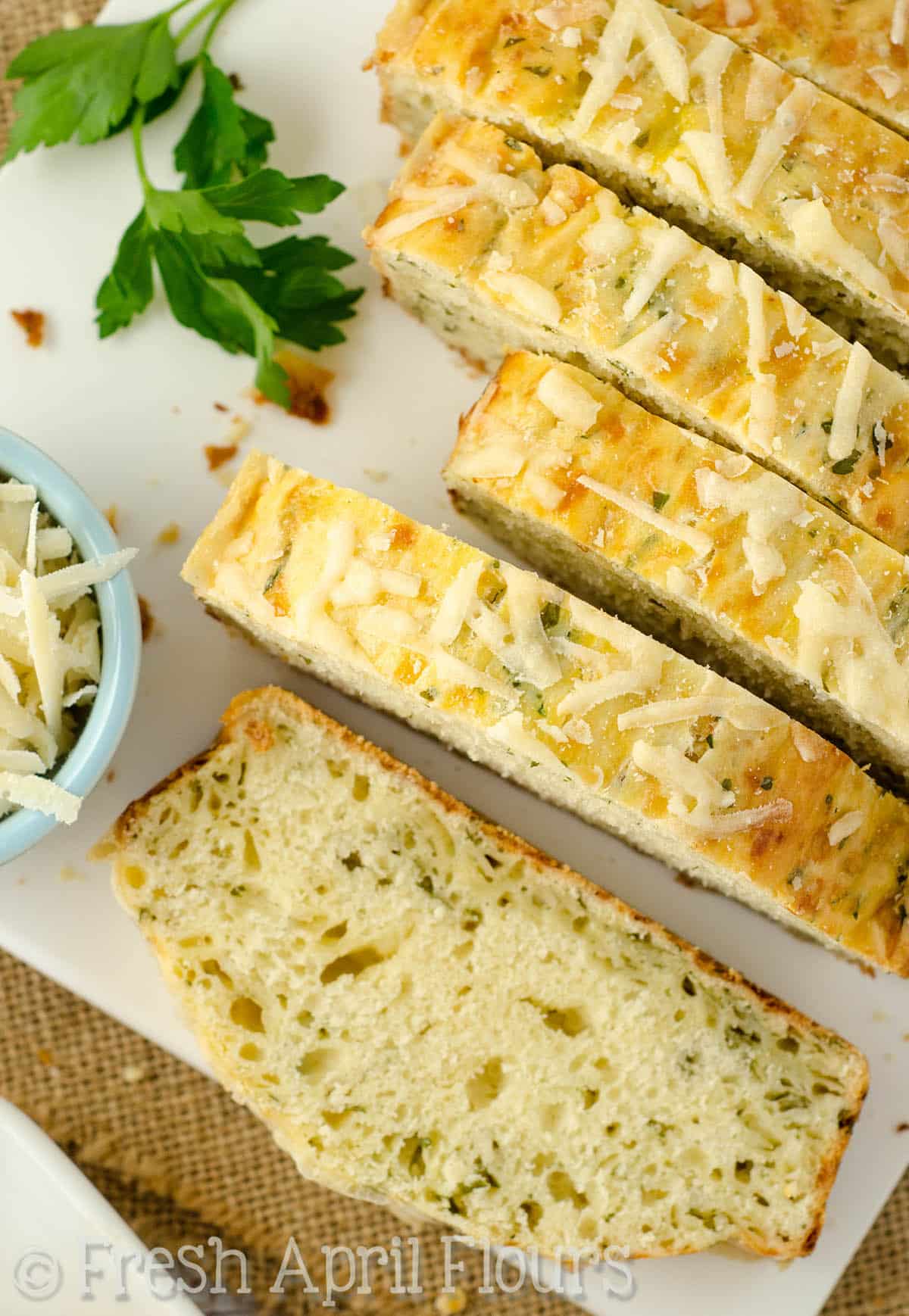 Sliced parmesan parsley bread on a cutting board.