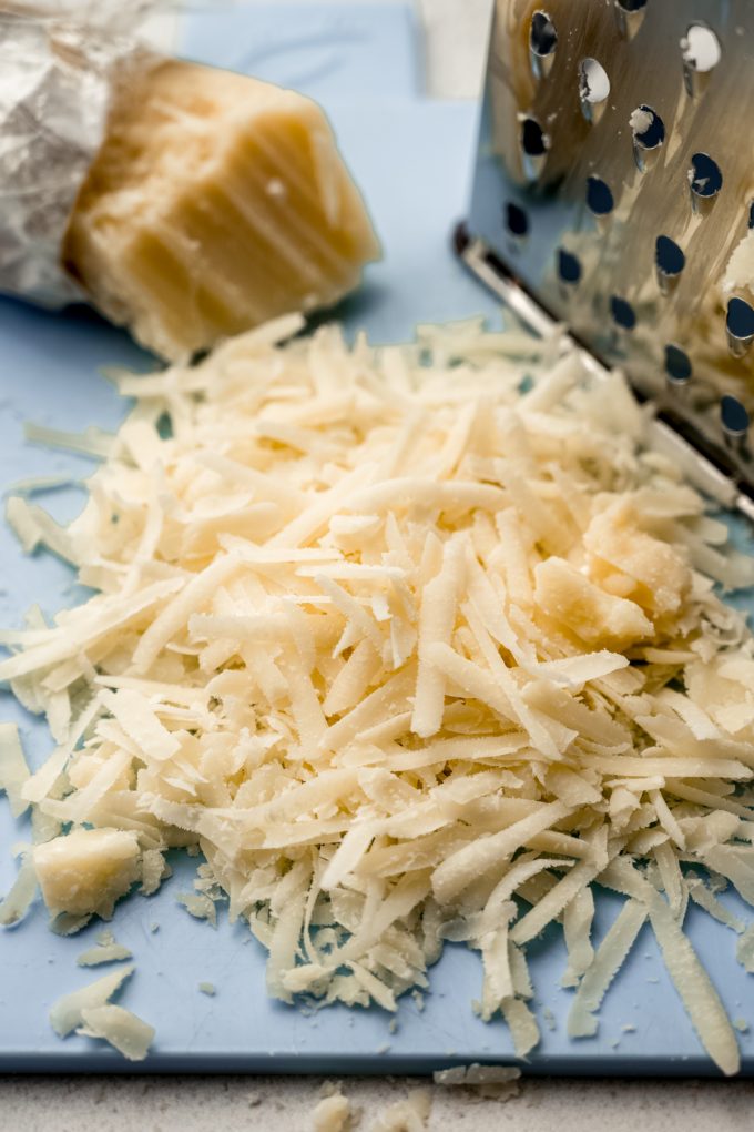 A pile of shredded Parmesan cheese on a blue cutting board.