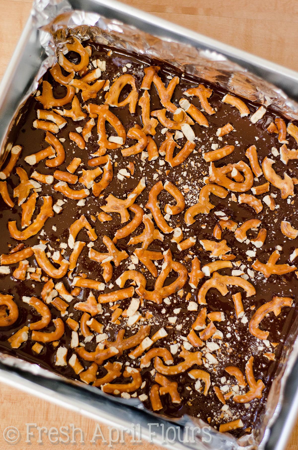 melted chocolate and pretzel pieces in a pan ready to make pretzel peppermint bark