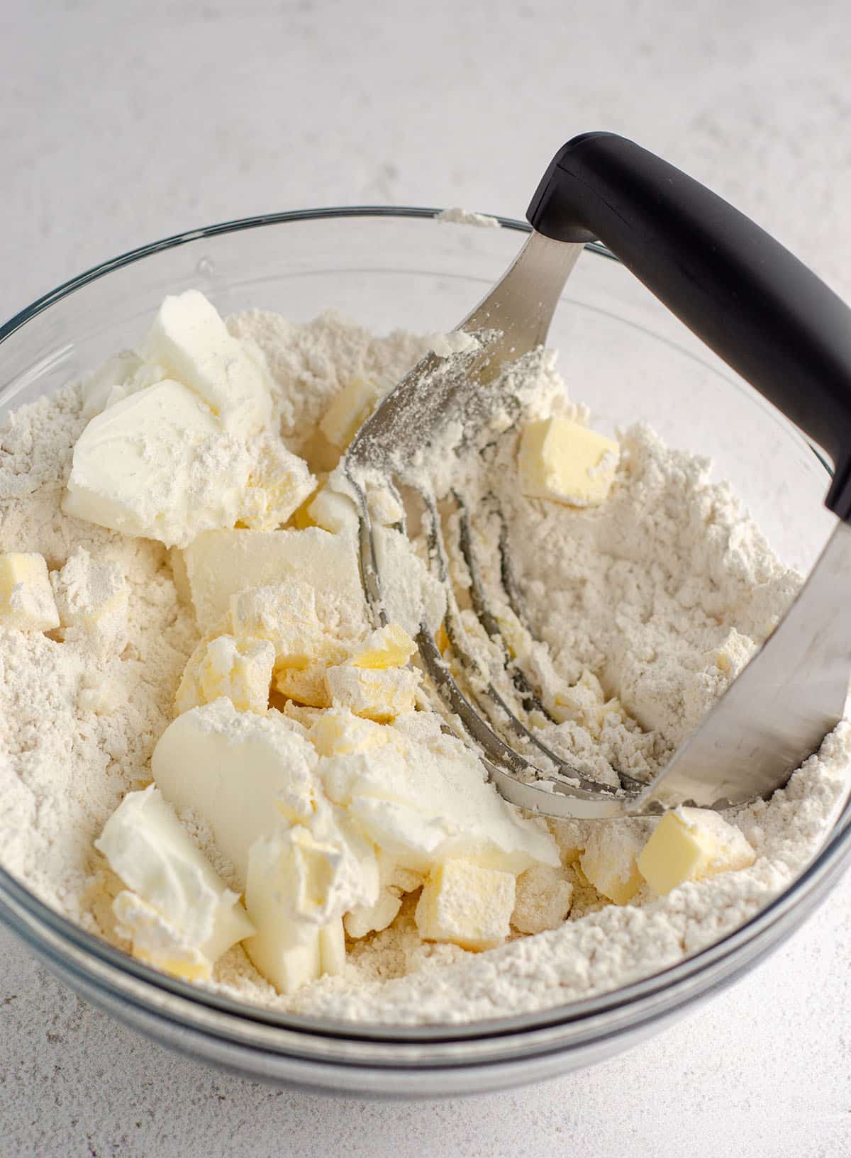 glass bowl with flour mixture, shortening, and butter being cut with a pastry cutter