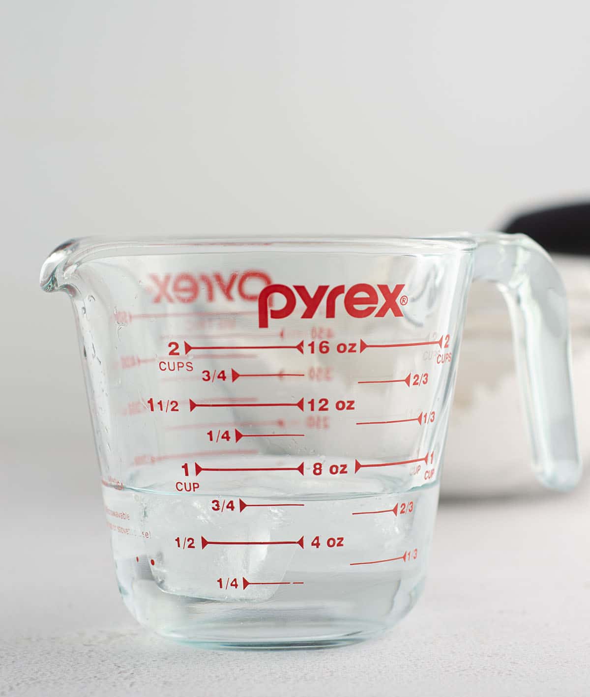 glass measuring cup of cold water with ice cubes