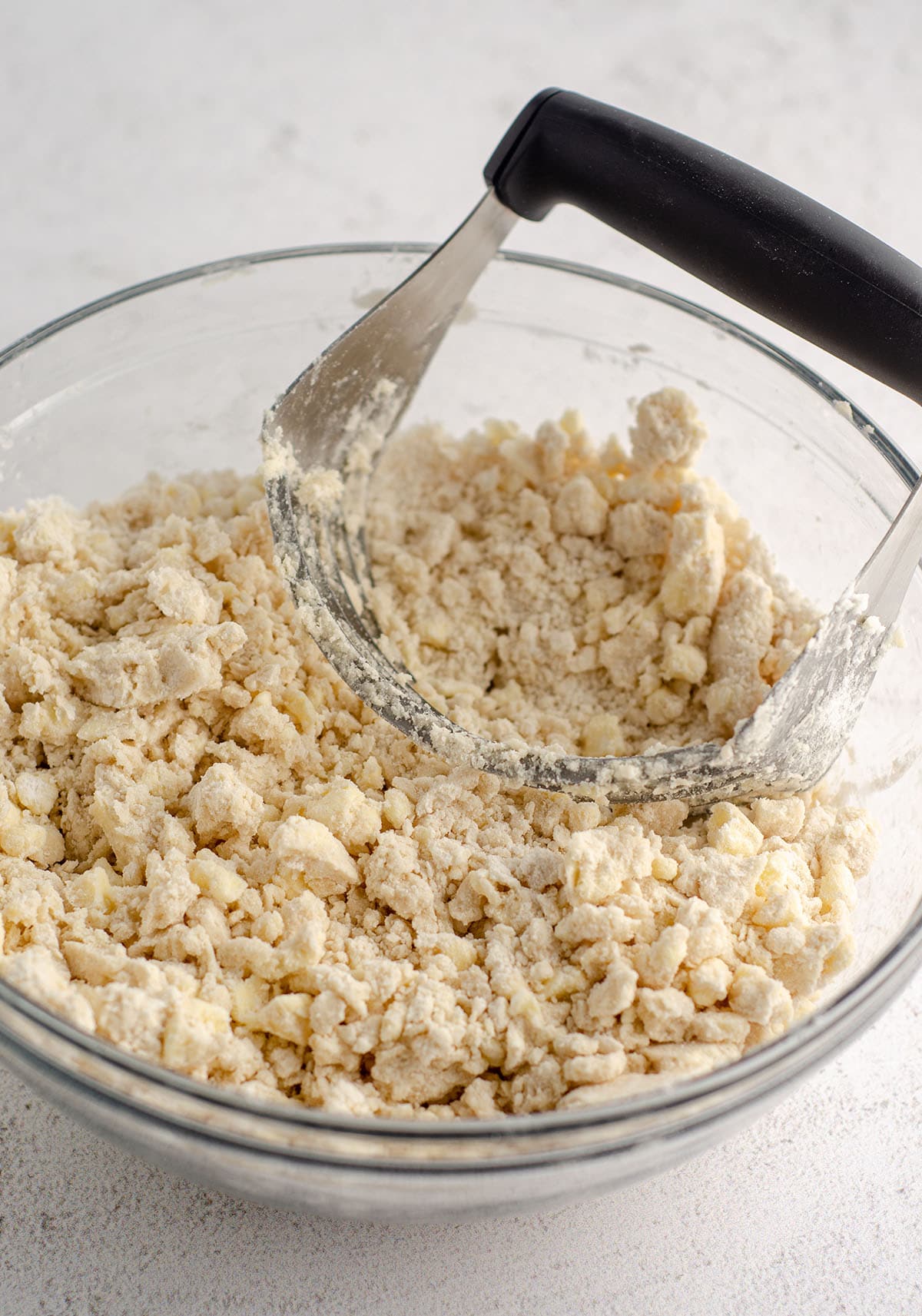 glass bowl with flour mixture, shortening, and butter being cut with a pastry cutter