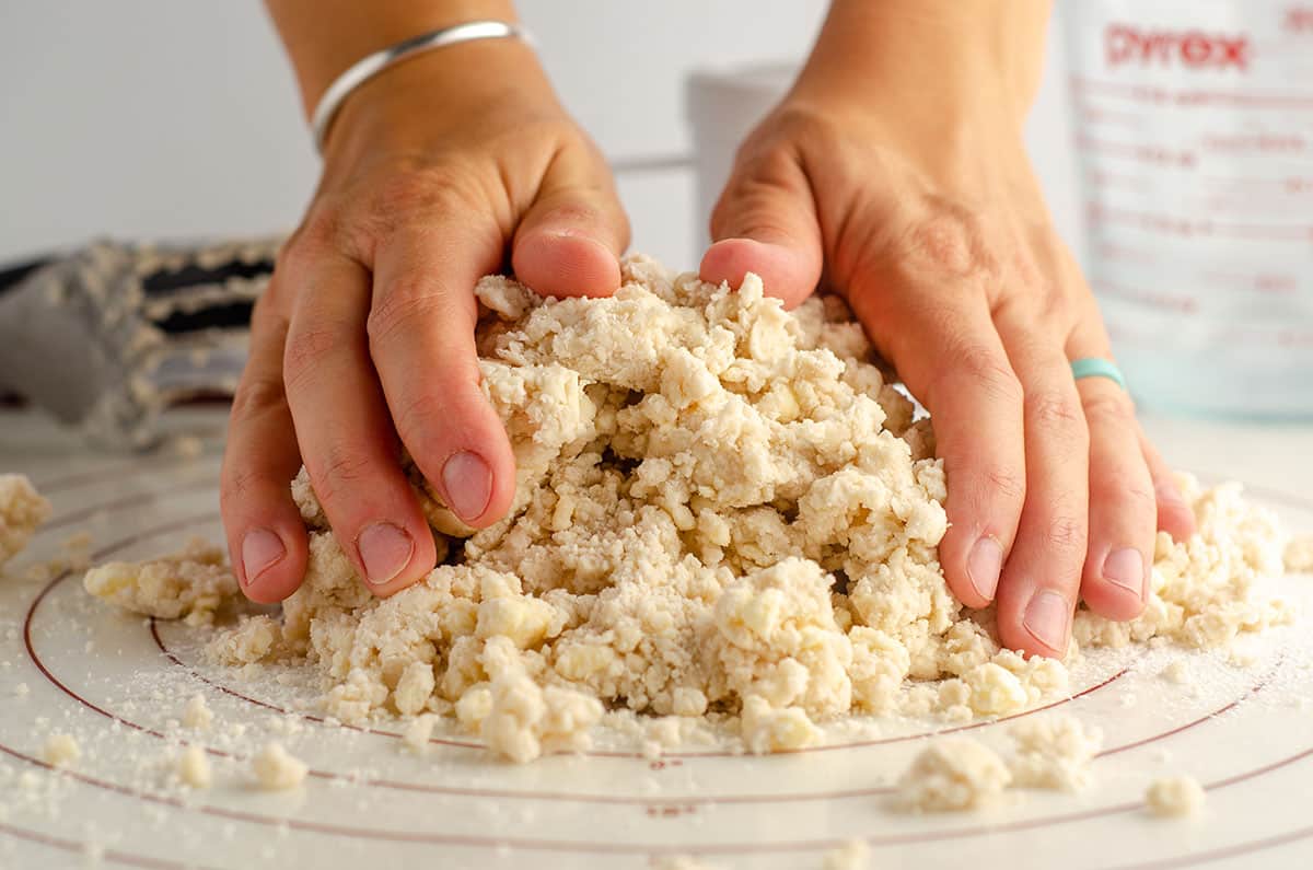 hands shaping crumbly pie dough on a pastry mat