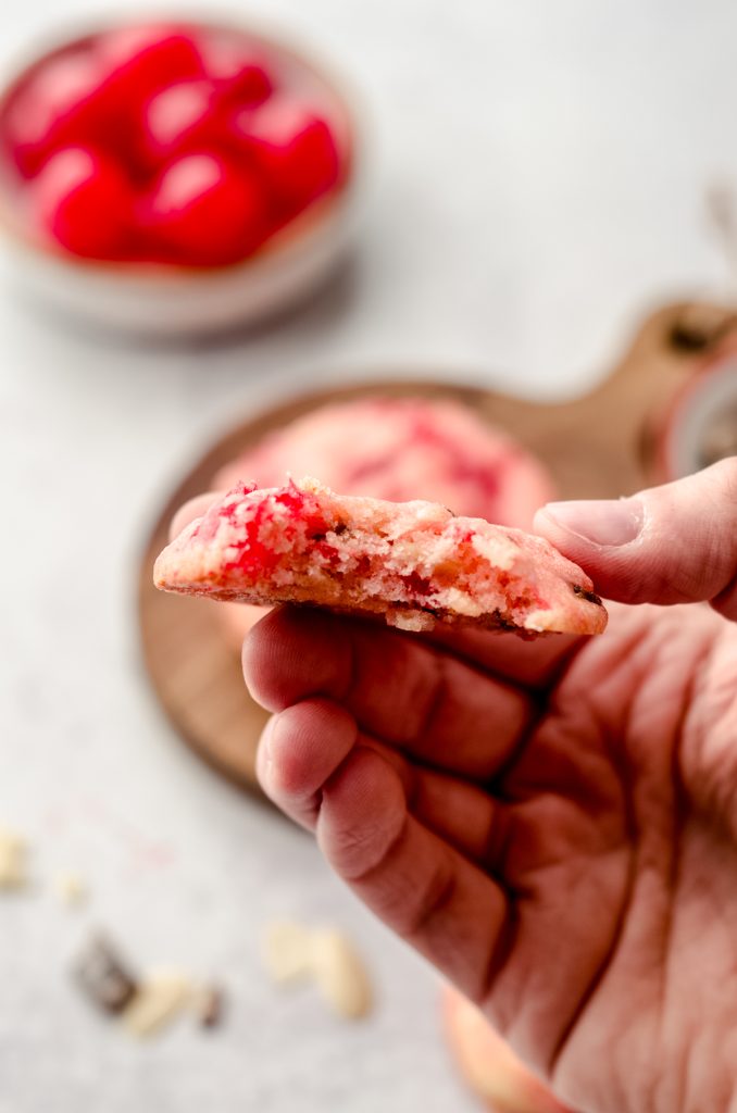 Someone is holding a cherry almond cookie with a bite taken out of it.
