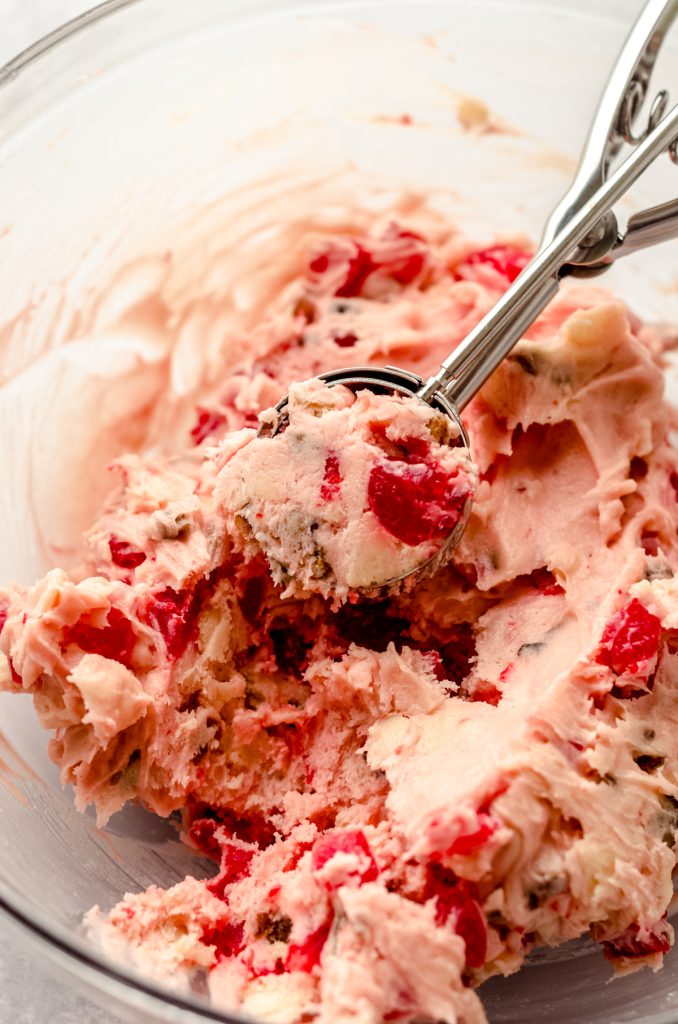 Cherry almond date cookie dough in a bowl with a cookie scoop.