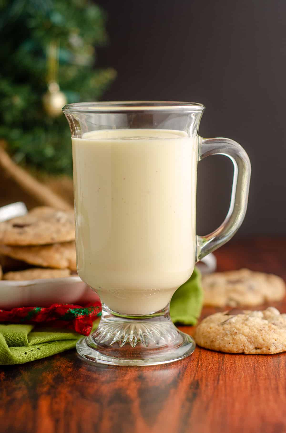 glass of eggnog with eggnog chocolate chunk cookies behind it