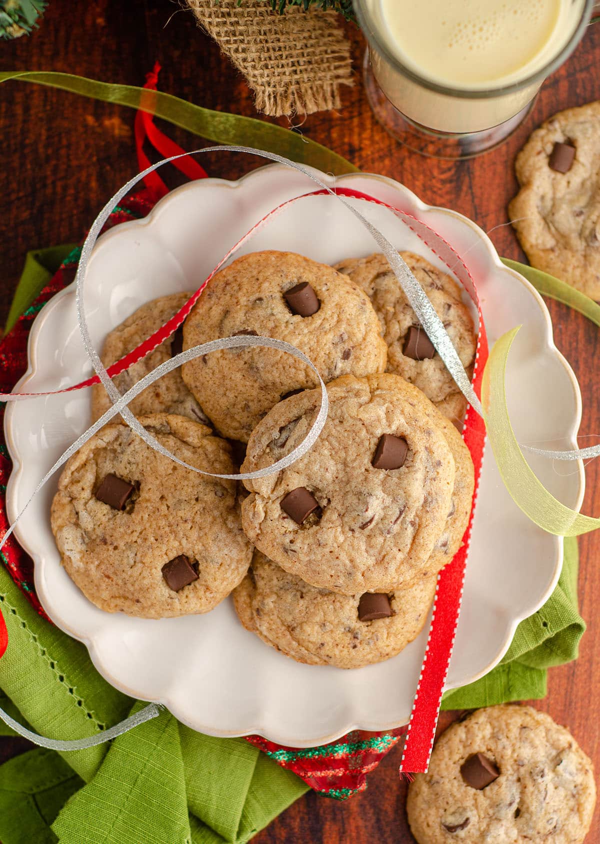 aerial photo of eggnog chocolate chunk cookies sitting on a plate with christmas ribbons around it