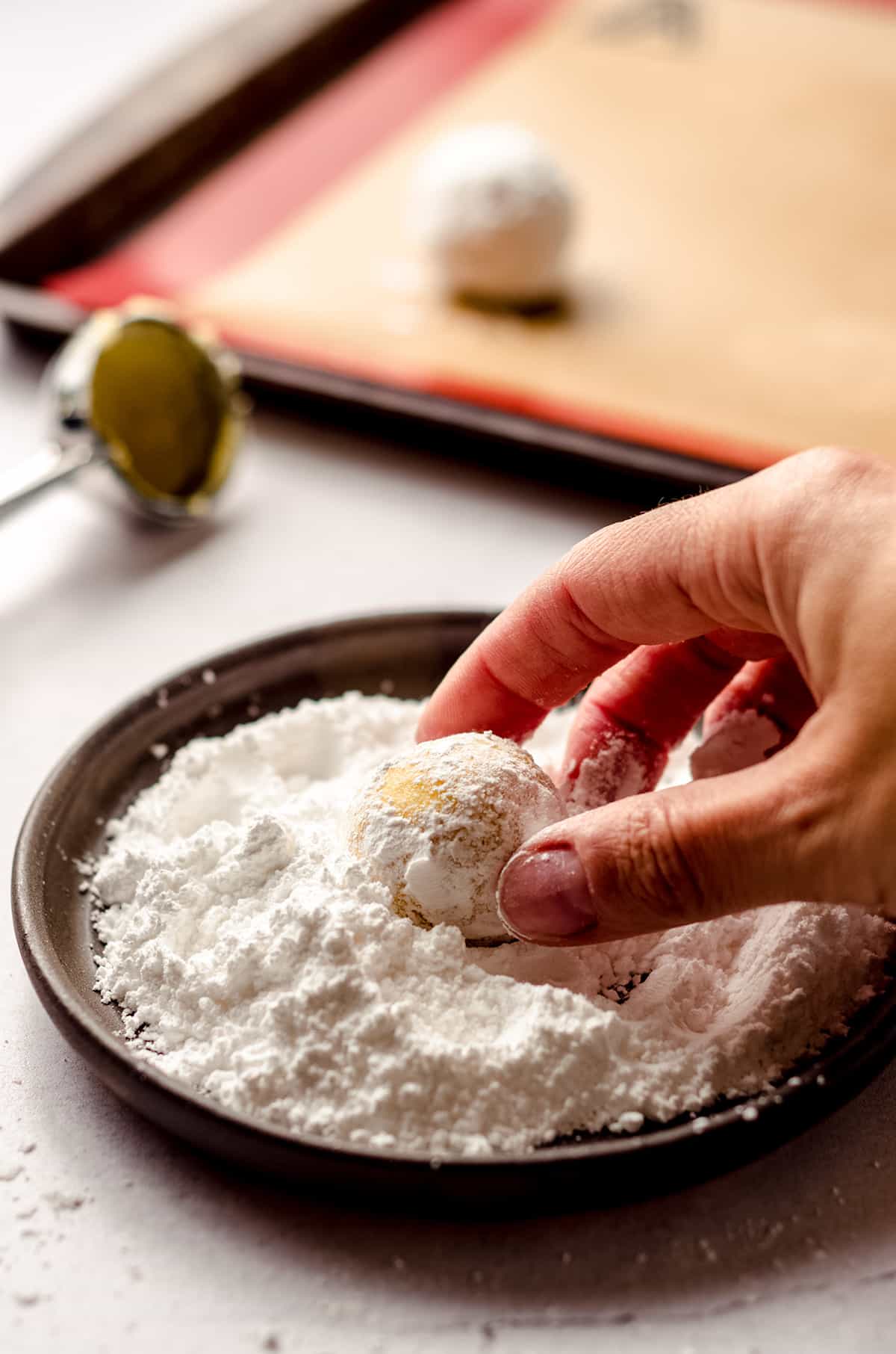hand rolling a lemon crinkle cookie dough ball in powdered sugar