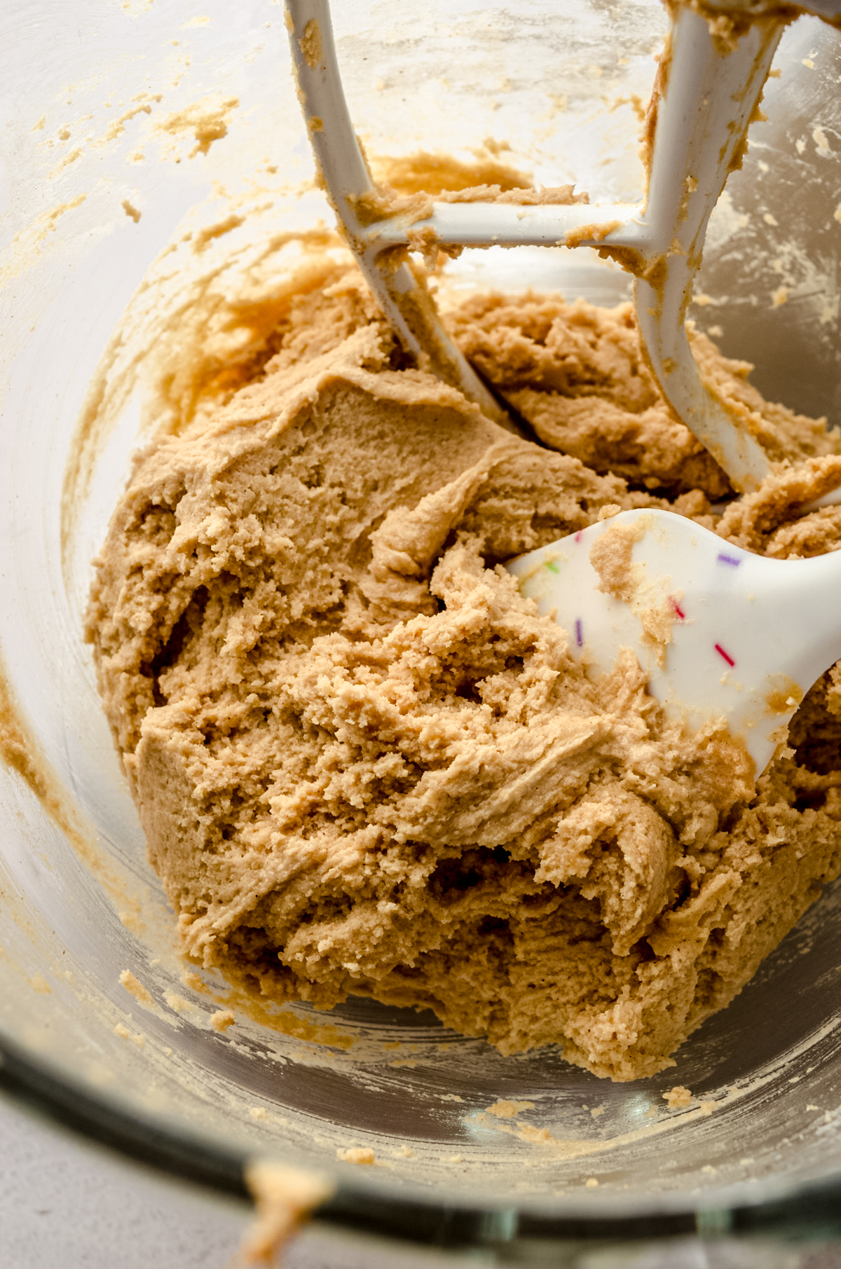 Cookie dough to make peanut butter blossoms in the bowl of a mixer with a spatula in it.