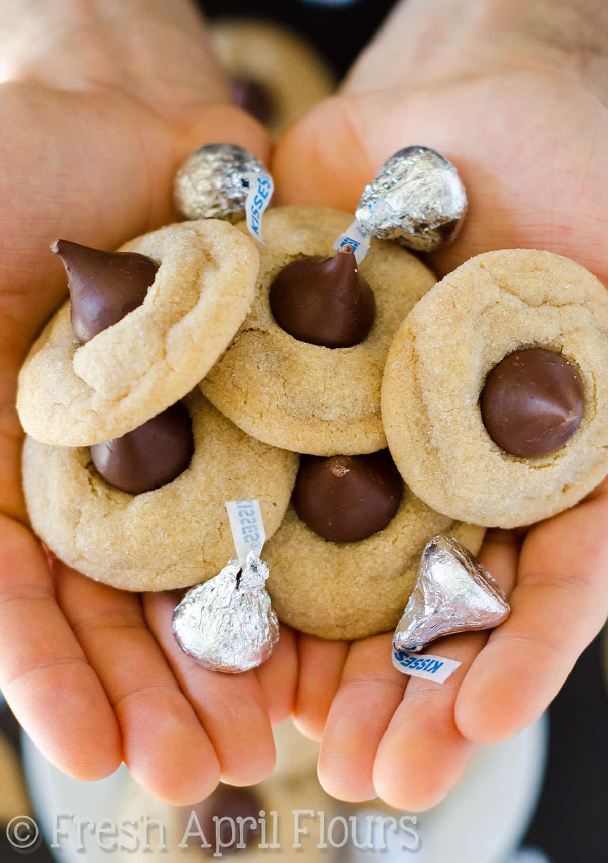 A man's two hands holding peanut butter blossom cookies and Hershey's Kisses.