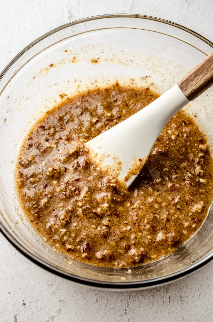 Pecan pie tart filling in a large glass bowl with a spatula.