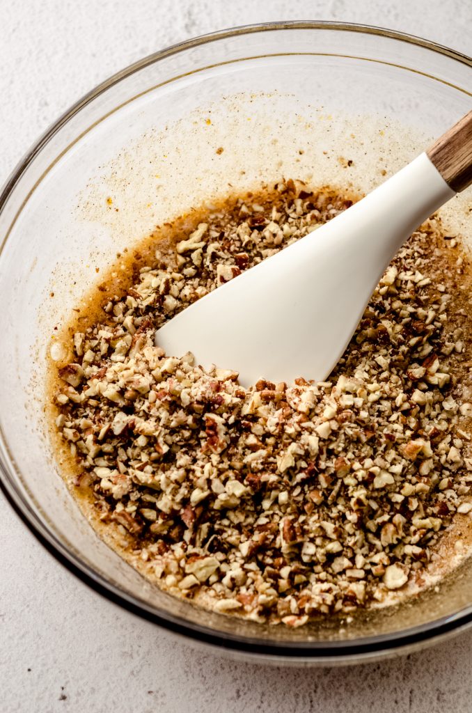 Pecan pie tart filling in a large glass bowl with a spatula.