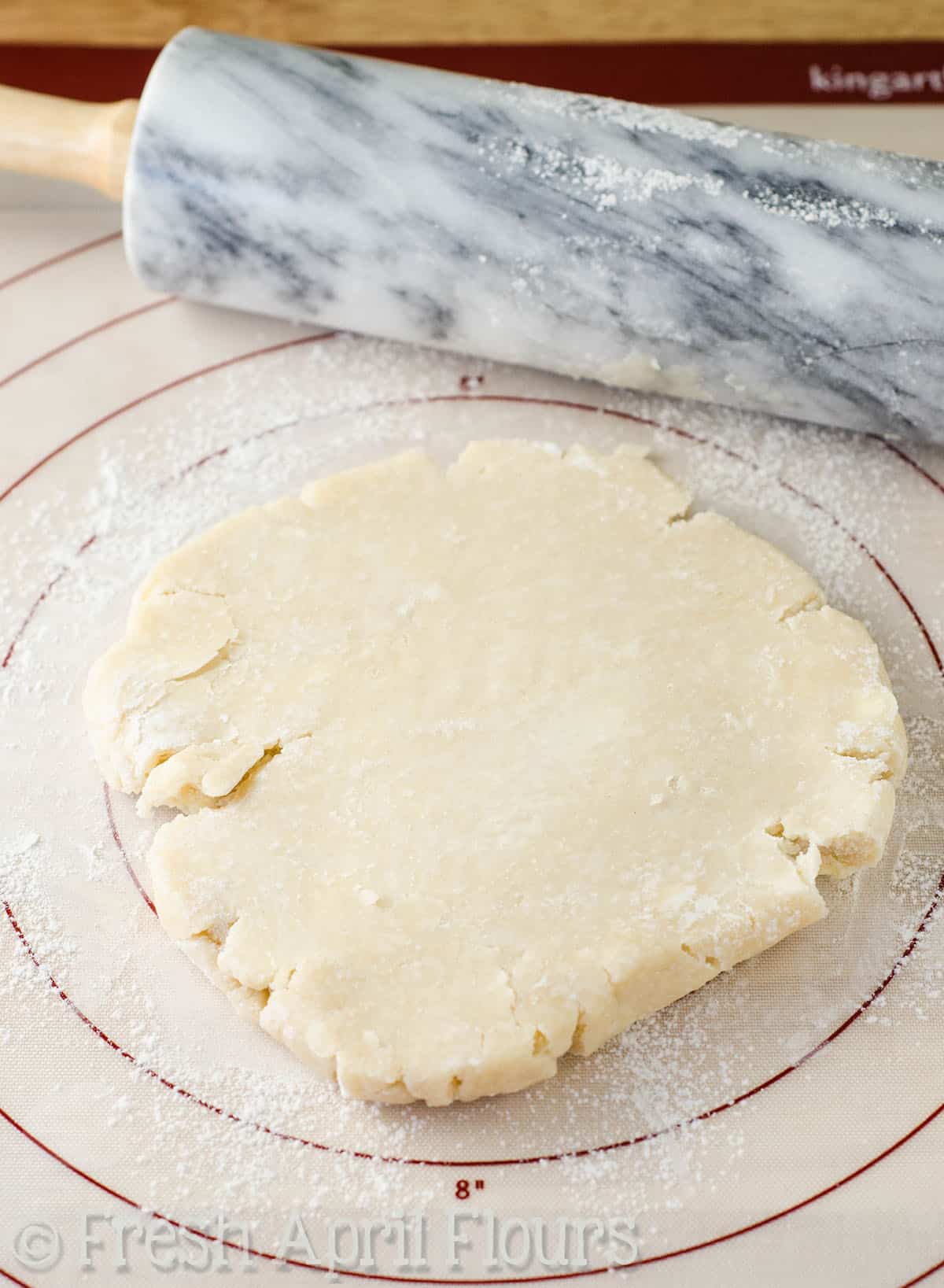 Pie crust on a baking mat with a rolling pin off to the side.