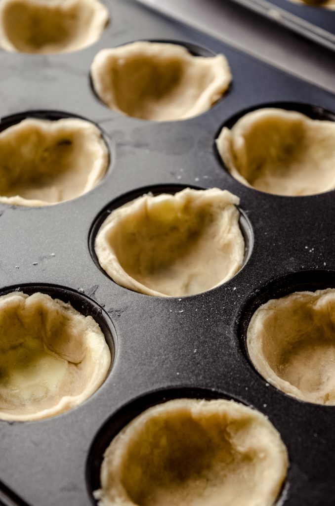 Unbaked pie dough circles pressed into a mini cupcake pan to make pecan tassies.