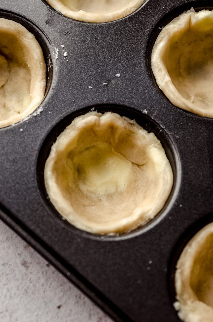 Unbaked pie dough circles pressed into a mini cupcake pan to make pecan tassies.