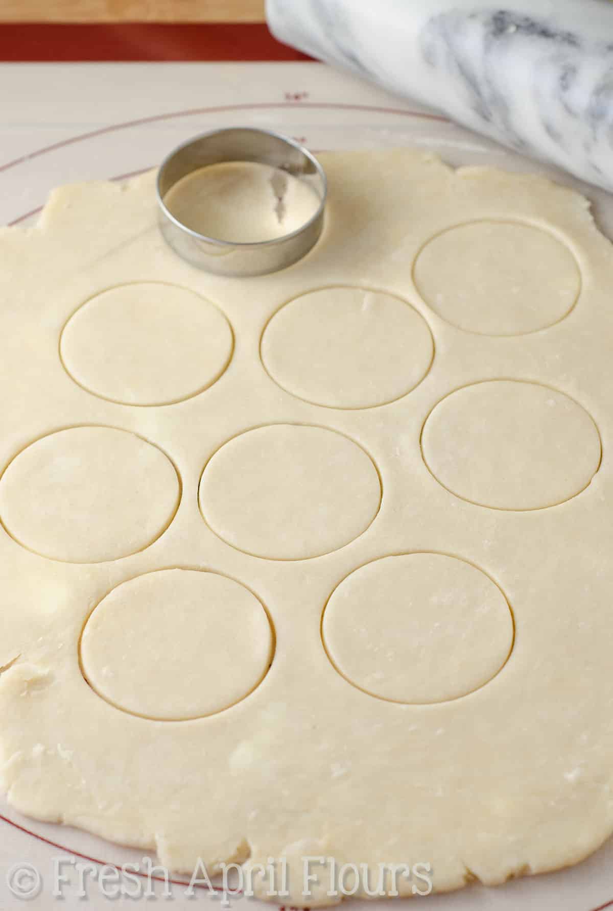 A circle cookie cutter cutting out circles from pie crust to make pecan pie tarts.