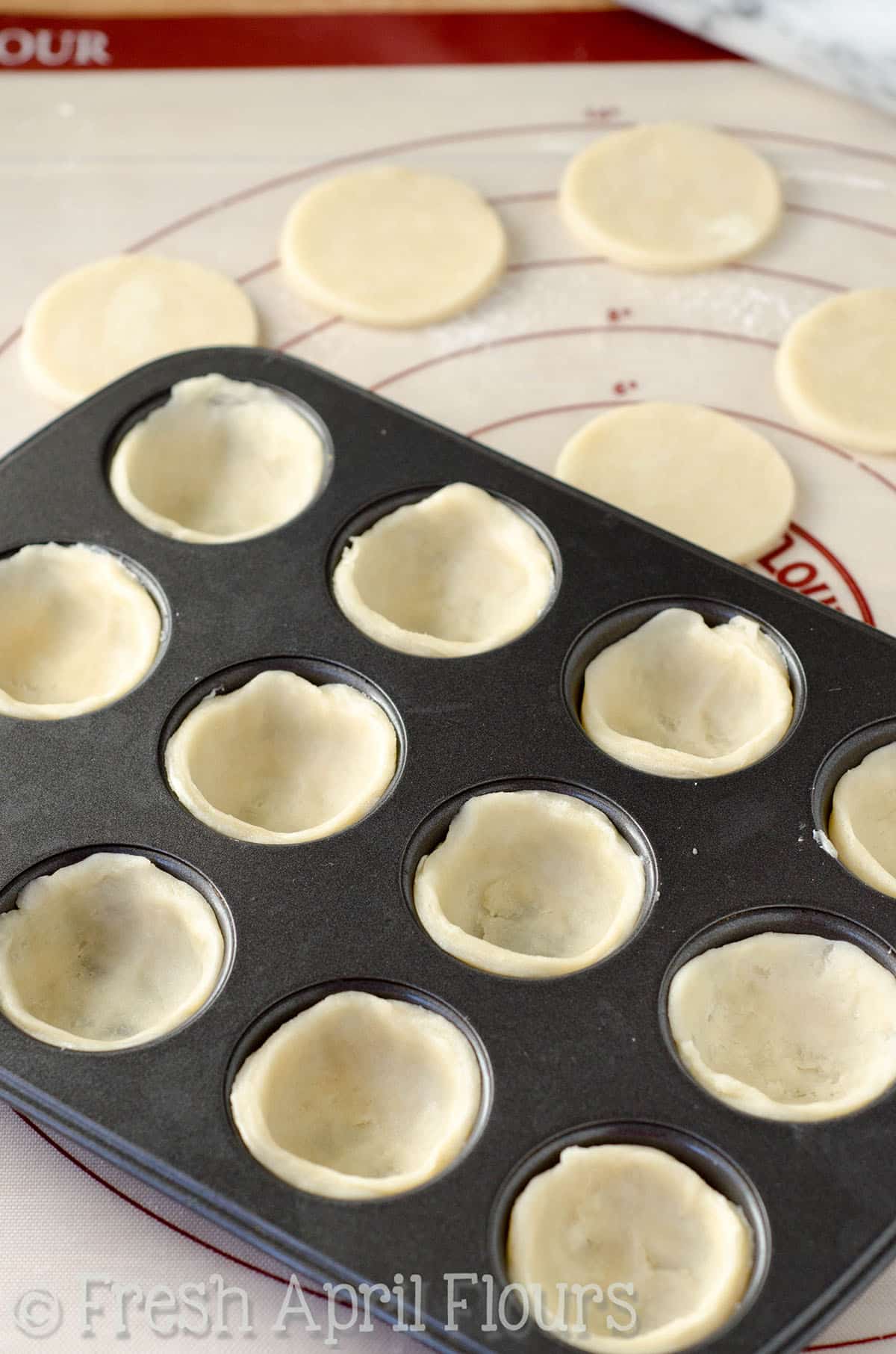 Pie crust circles pressed into a mini cupcake pan to make pecan pie tarts.