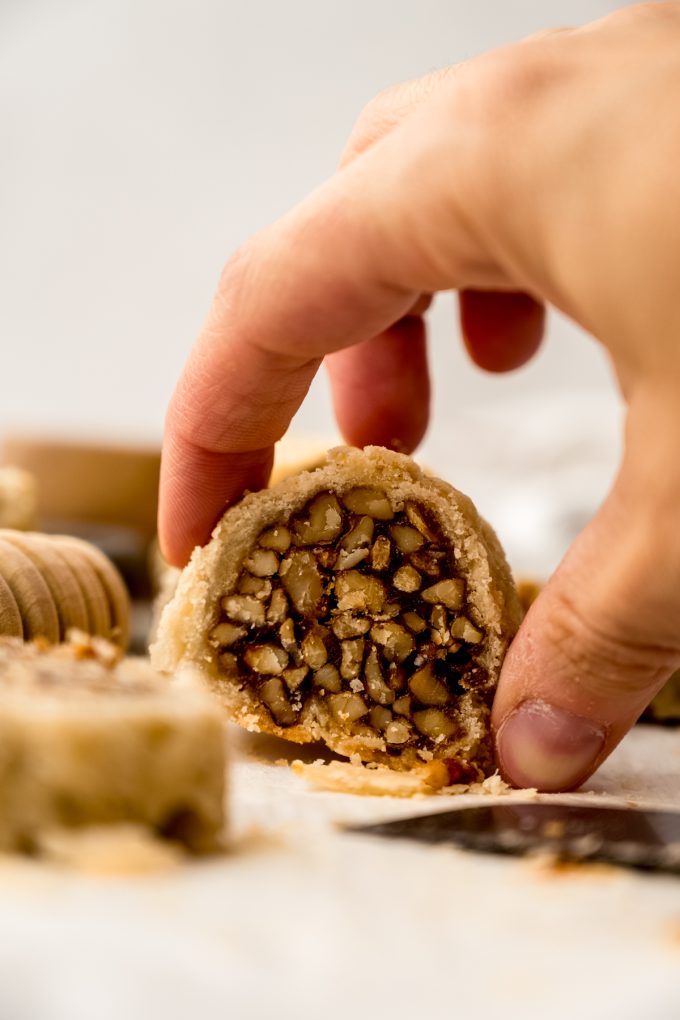 Someone is grabbing a honey walnut cookie stick slice (sfratti) from a surface.