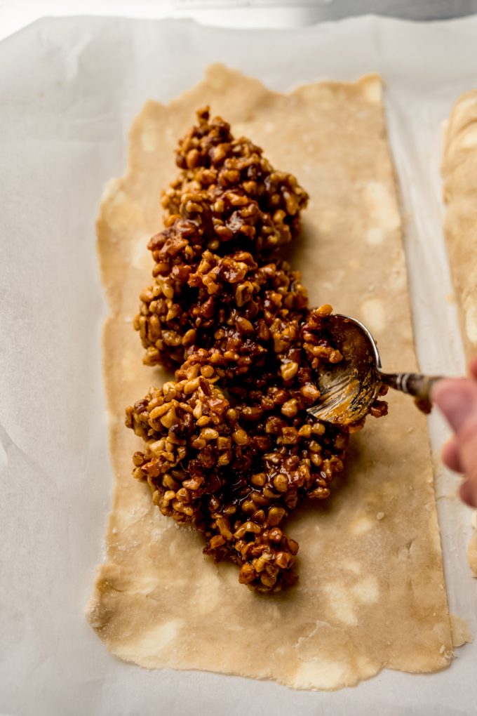 Someone is spooning honey walnut cookie stick filling onto a pie dough.