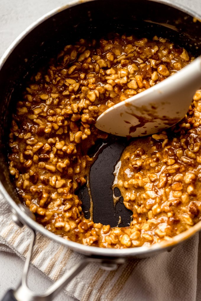 A saucepan of the filling for honey walnut cookie sticks that someone is stirring with a spatula.