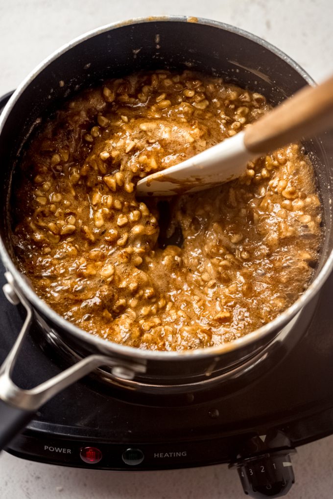 A saucepan of the filling for honey walnut cookie sticks that someone is stirring with a spatula.