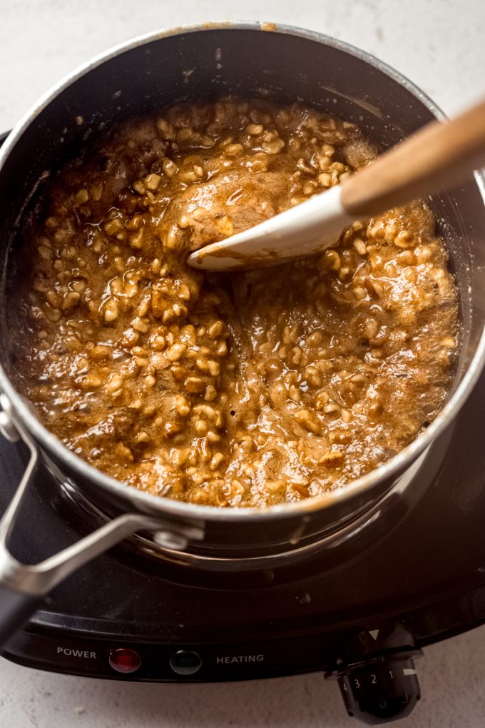 A saucepan of the filling for honey walnut cookie sticks that someone is stirring with a spatula.