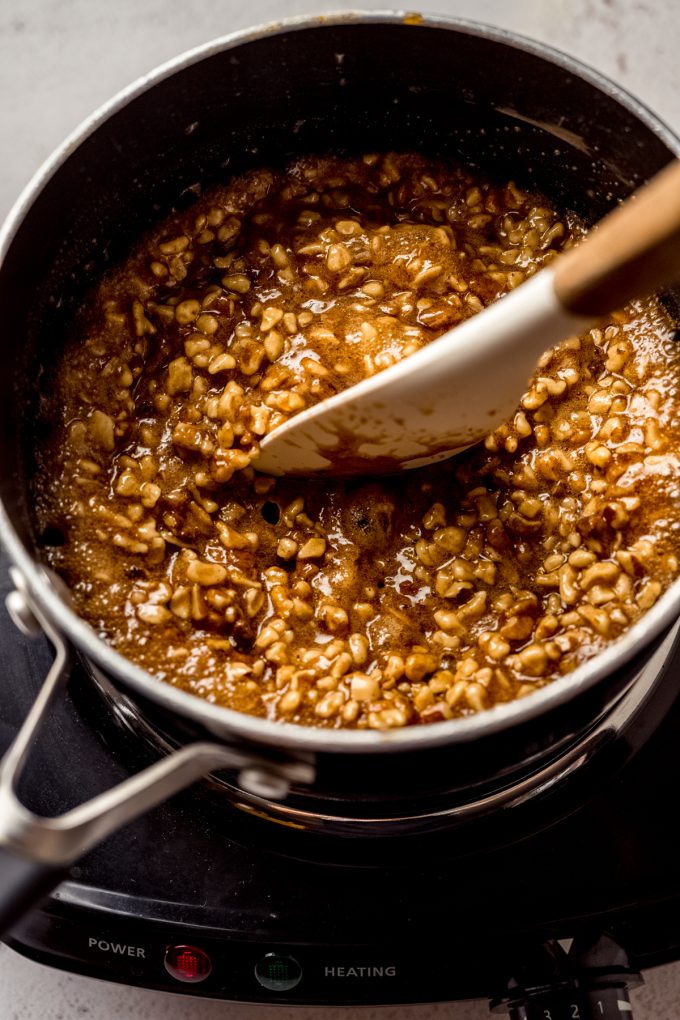 A saucepan of the filling for honey walnut cookie sticks that someone is stirring with a spatula.