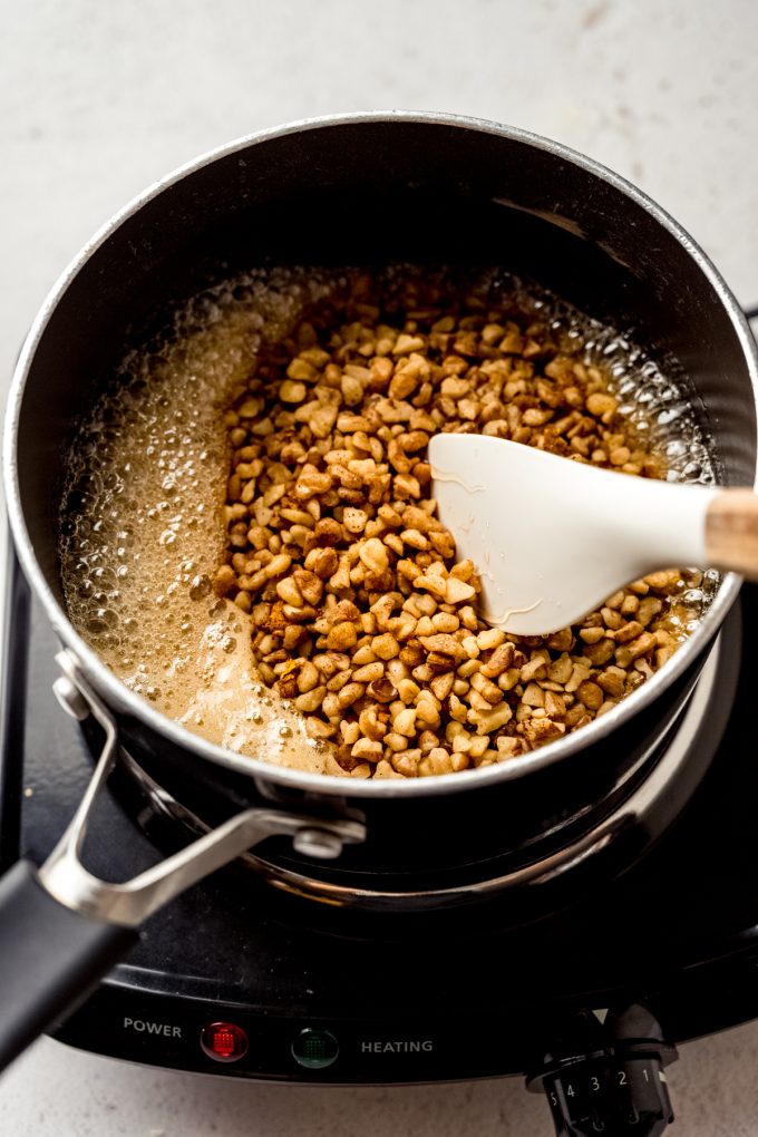 A saucepan of the filling for honey walnut cookie sticks that someone is stirring with a spatula.