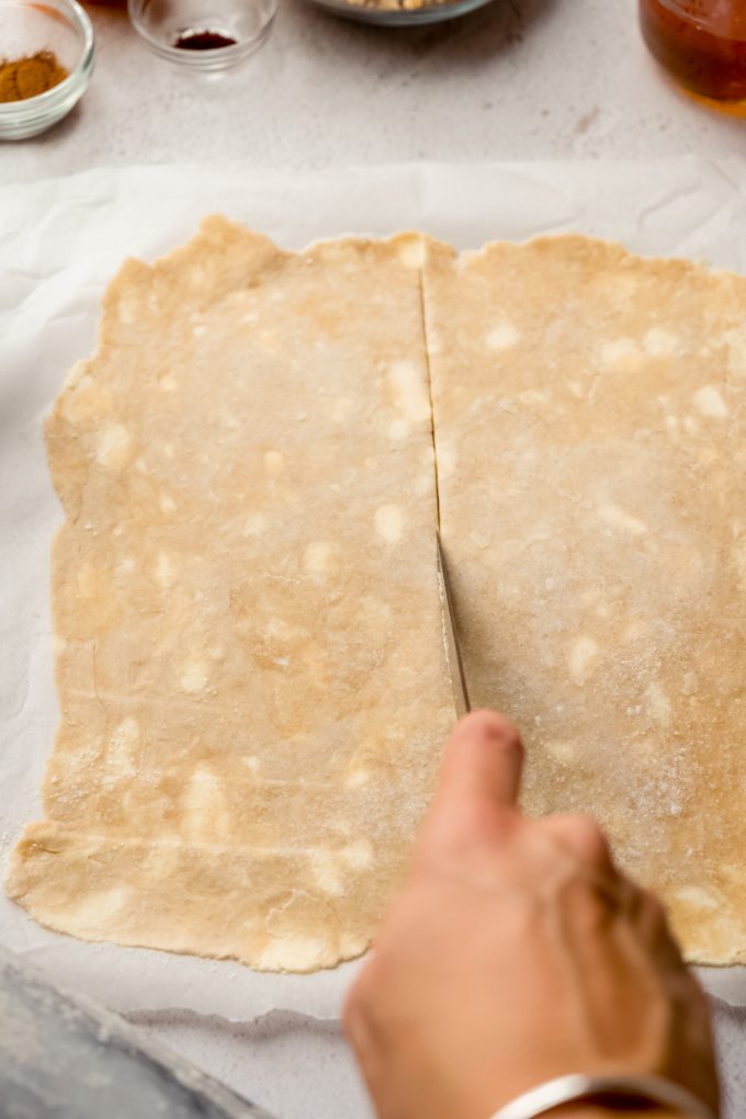 Someone is slicing a square of pie dough in half with a pizza cutter.