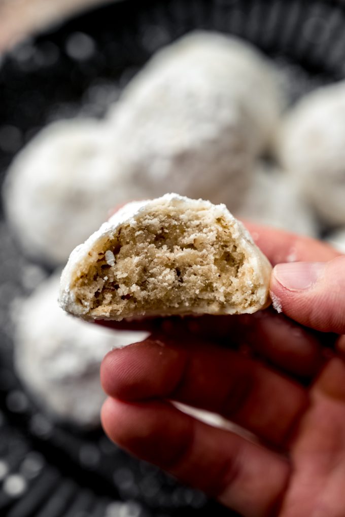 Someone is holding a Russian tea cake that has had a bite taken out of it.