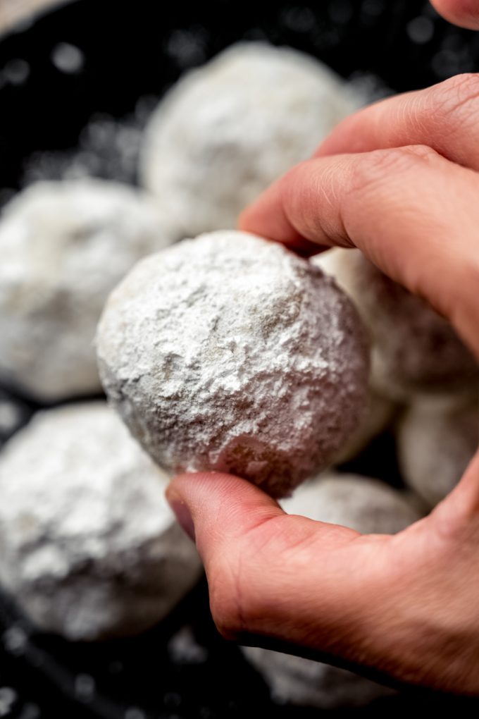 Someone is holding a snowball cookie between their thumb and pointer finger.
