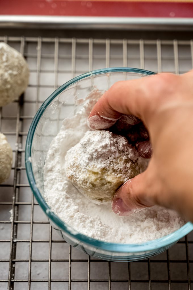 Someone is rolling a snowball cookie in a bowl of powdered sugar.