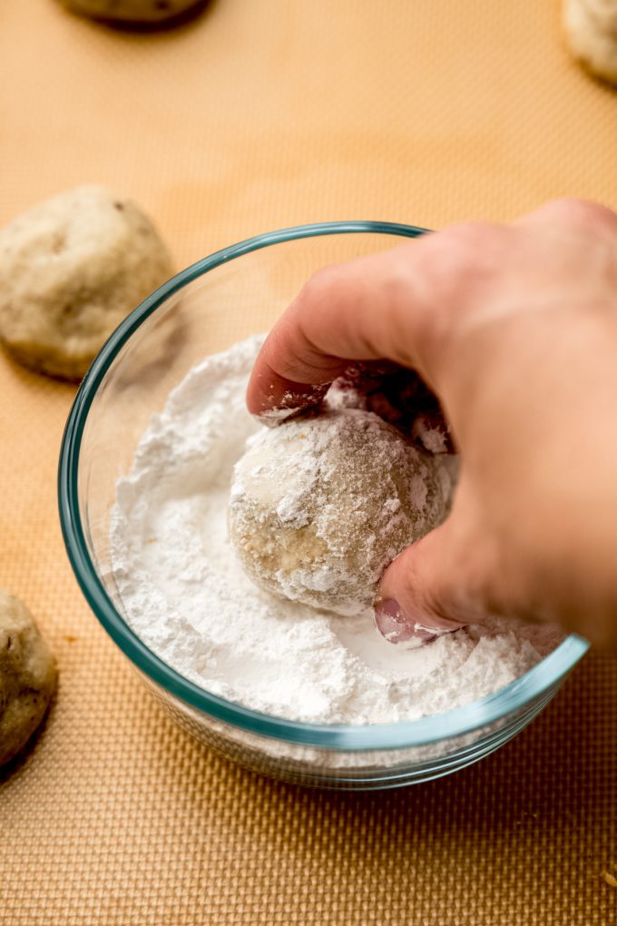 Someone is rolling a snowball cookie in a bowl of powdered sugar.