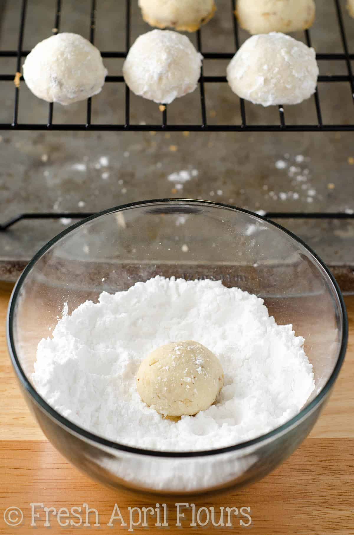 russian tea cakes cookie dough balls getting rolled in powdered sugar