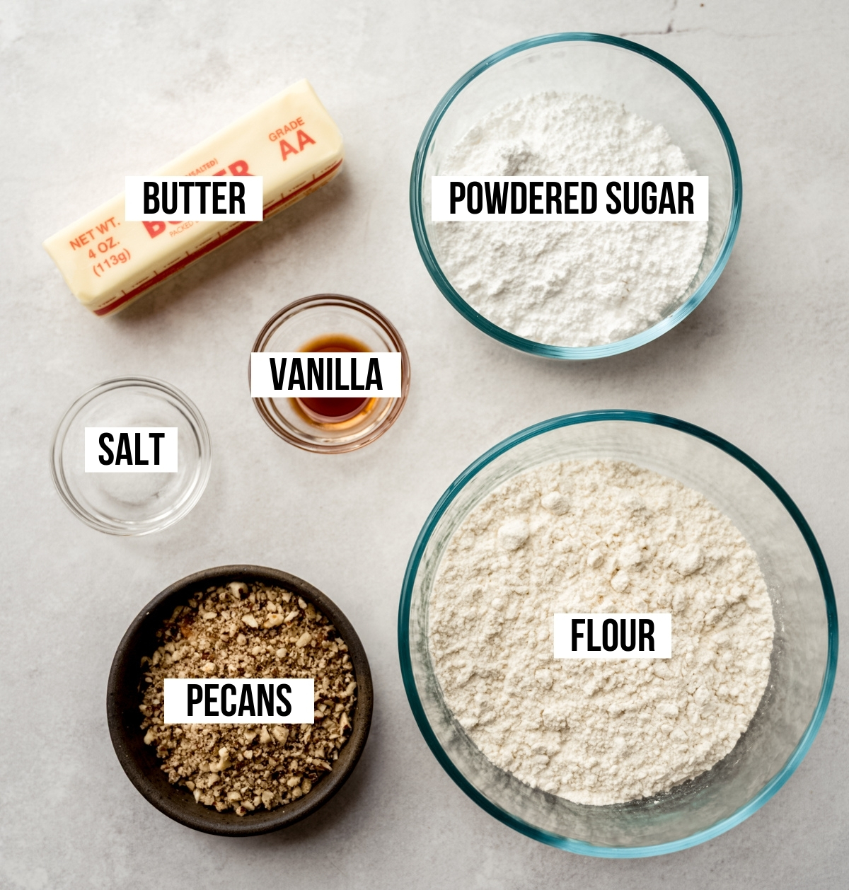 Aerial photo of ingredients to make Russian tea cakes (snowballs) with text overlay labeling each ingredient.