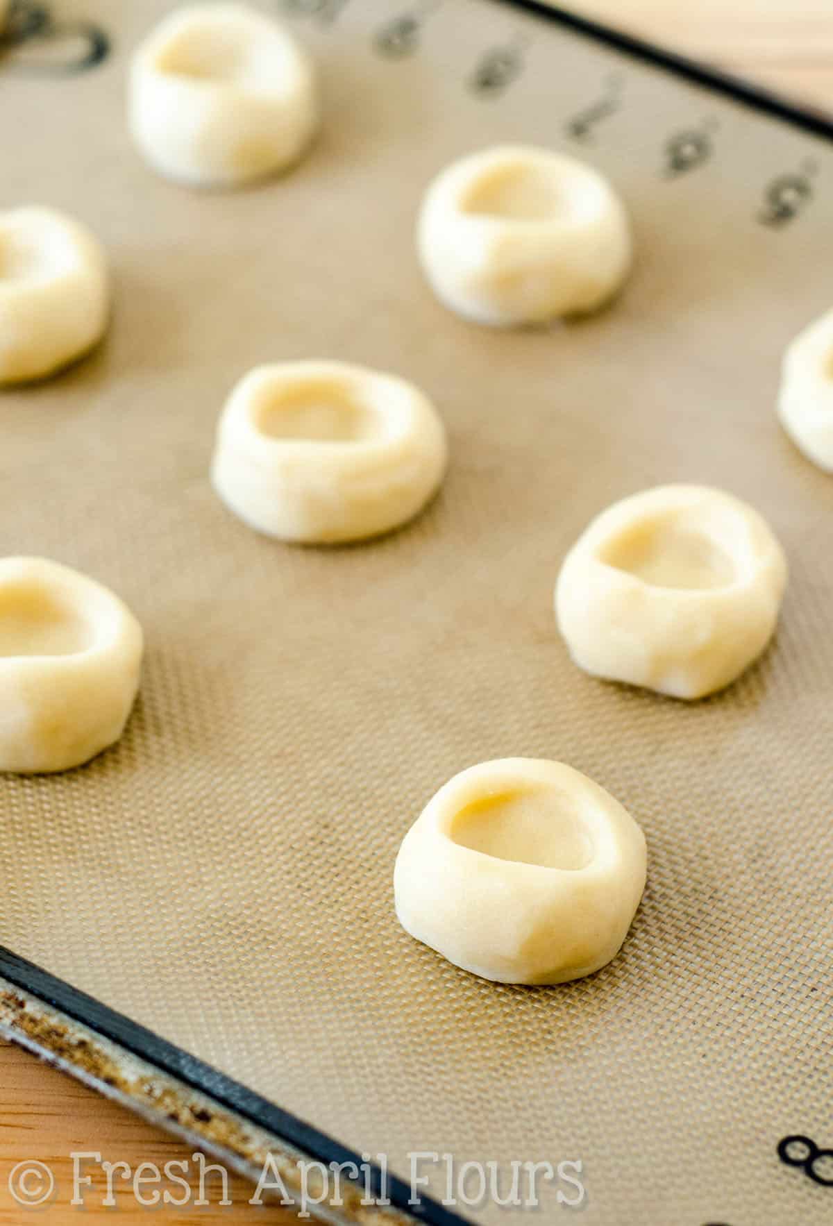 Thumbprint cookie dough with imprints in them on a baking sheet.