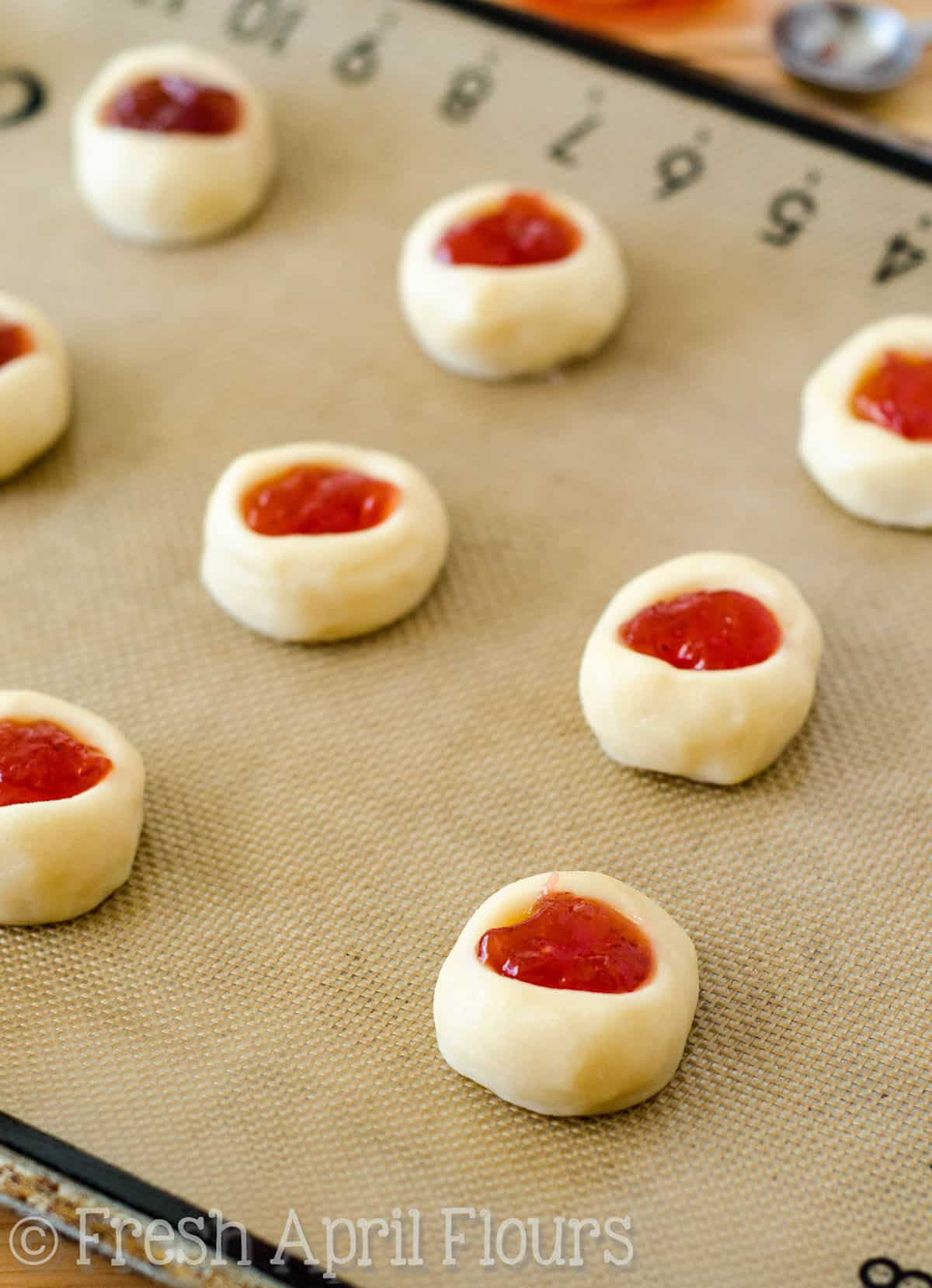 Thumbprint cookies with jam in them on a baking sheet ready to bake.