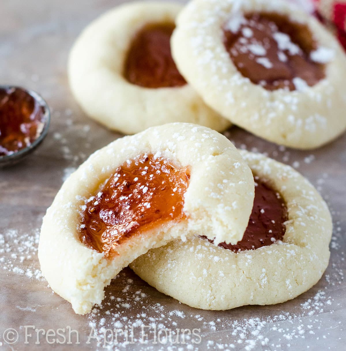 Thumbprint cookies on a surface and a bite taken out of one.