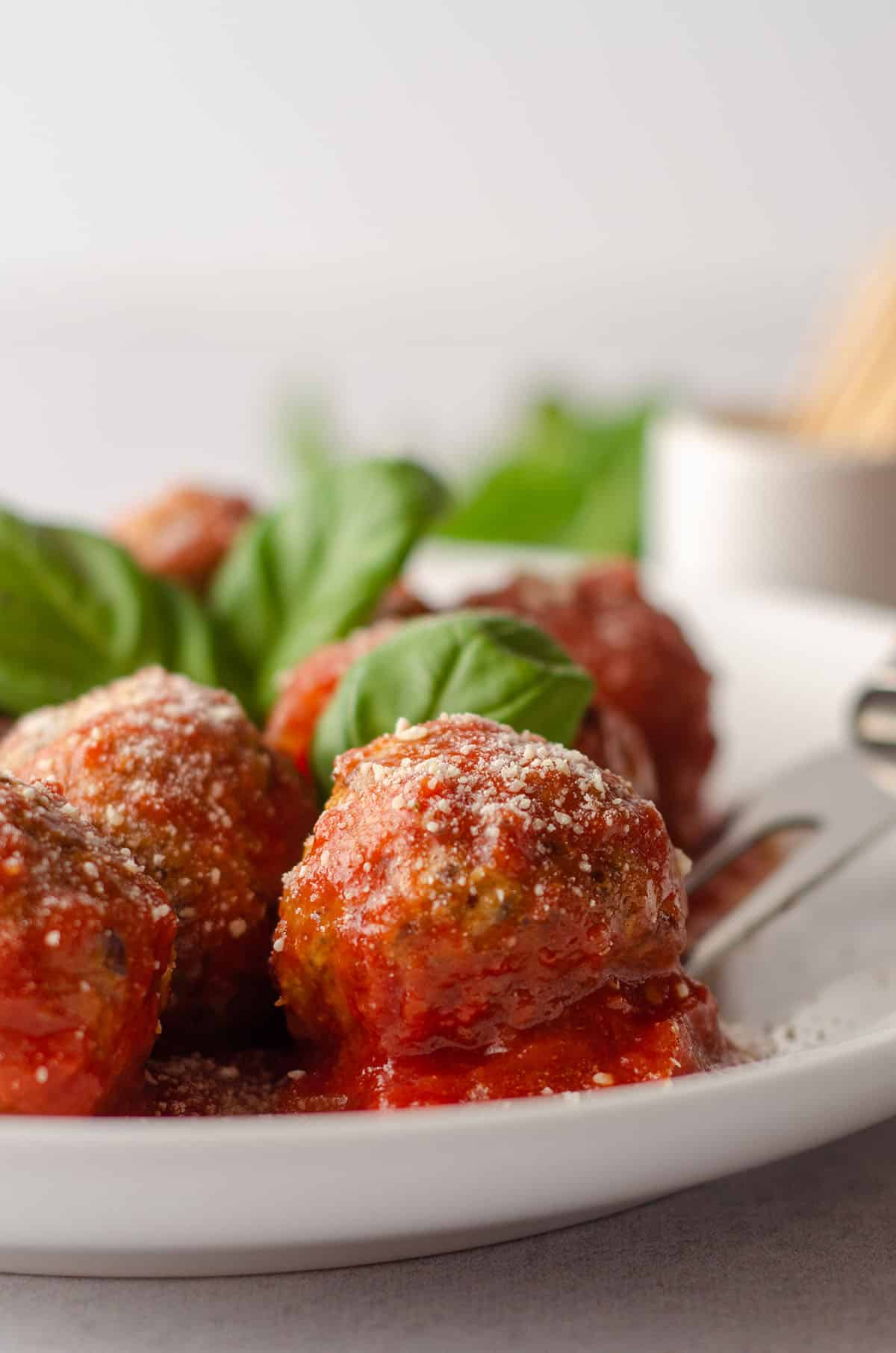 gluten free meatballs on a plate with basil leaves and a serving fork