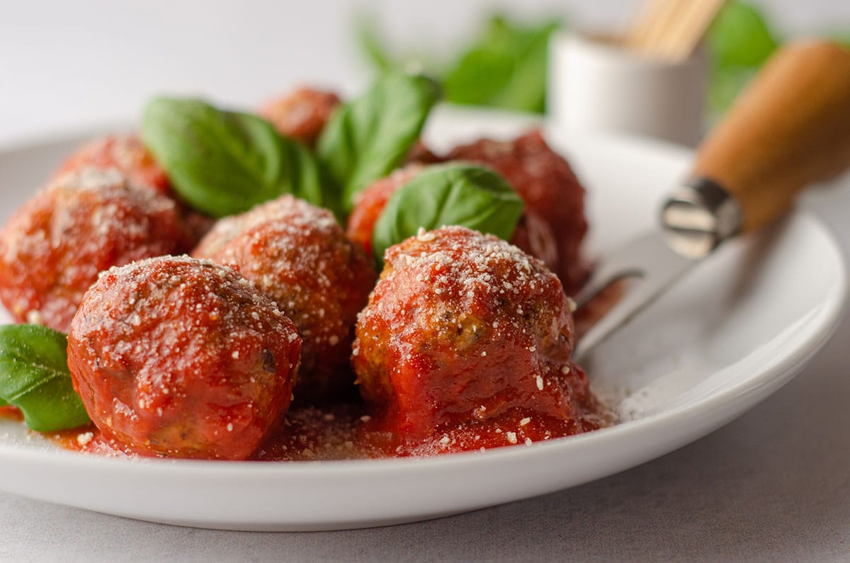 gluten free meatballs on a plate with basil leaves and a serving fork